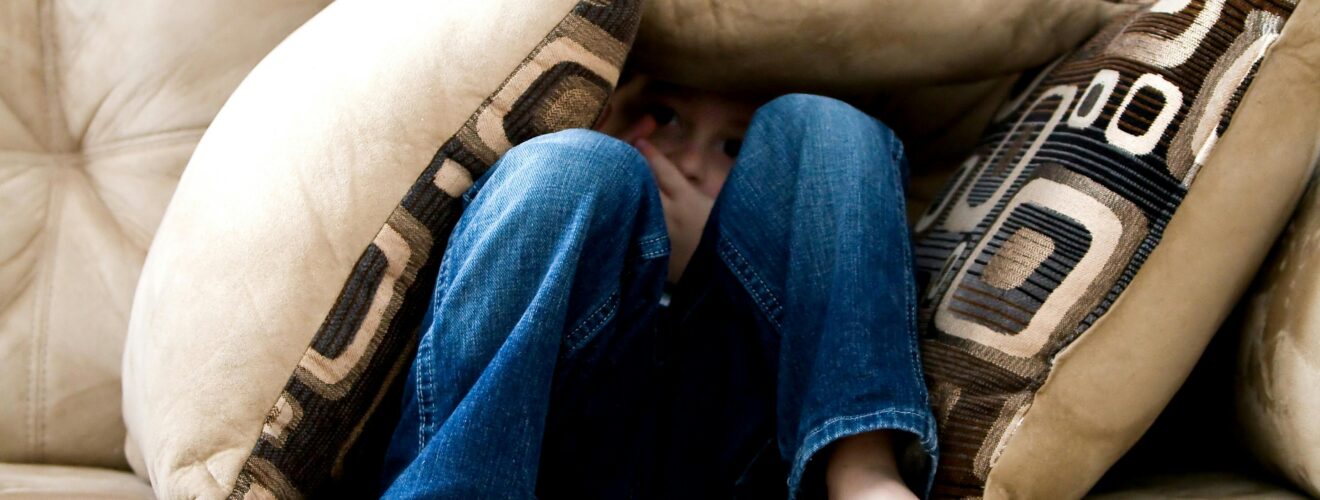 A child crouched under cushions on a couch, conveying a sense of playfulness or fear.