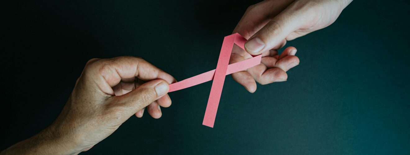 Two hands exchanging a pink ribbon symbolizing breast cancer awareness and support.