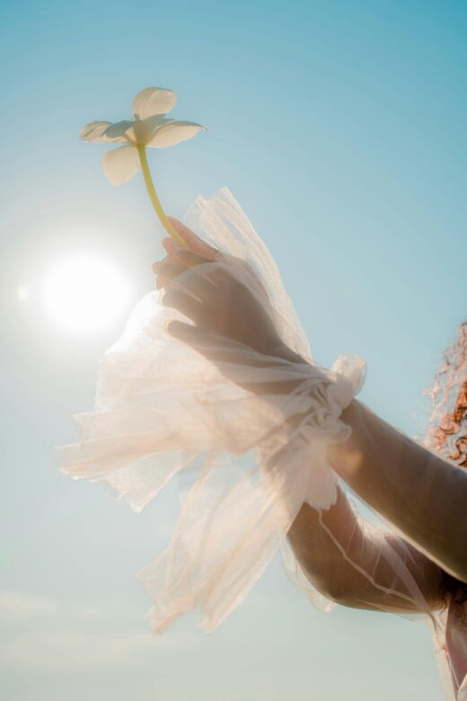 Graceful hands holding a flower against a sunny clear sky, capturing elegance and freedom.