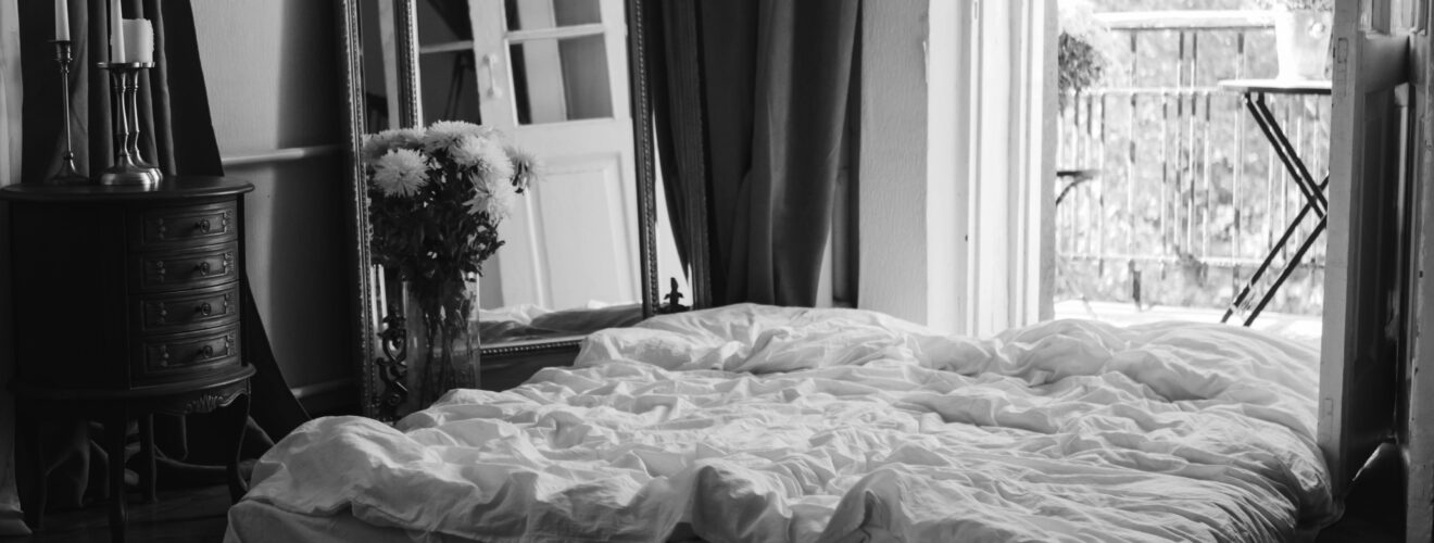 Black and white image of a stylish bedroom with a balcony view, cozy bed, and elegant decor.