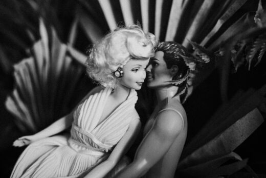 Vintage-style black and white photo of Barbie and Ken dolls in a romantic embrace amidst foliage.